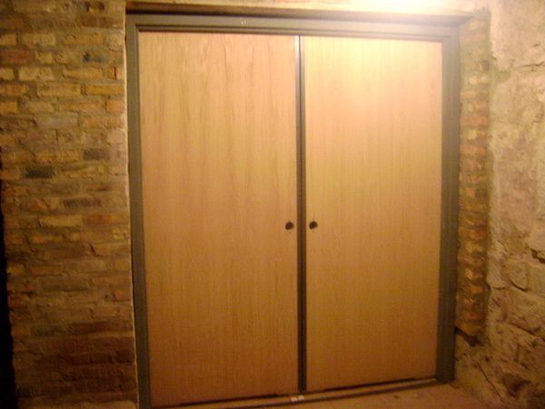 A wooden door is in a room with a brick wall.