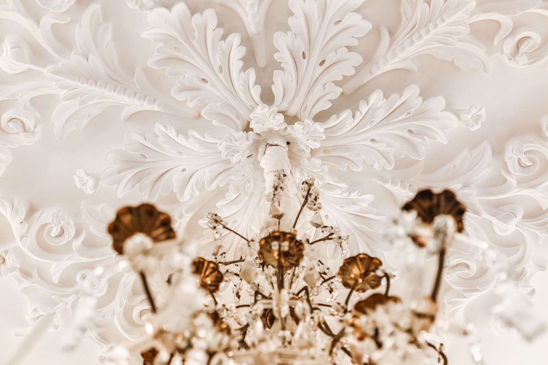 Ornate white plaster ceiling detail with a crystal chandelier below.
