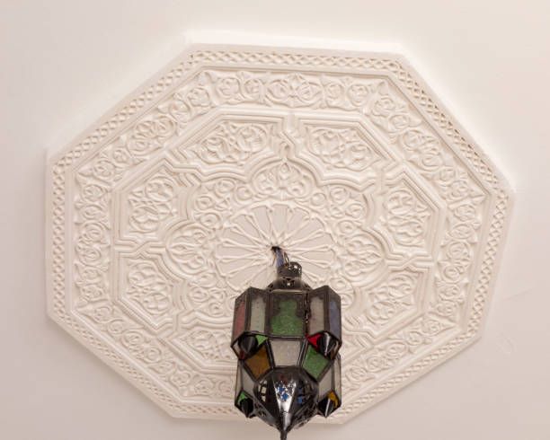 Octagonal white ceiling medallion with intricate relief patterns. A colorful glass and metal hanging lamp is below.