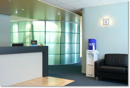 Reception area with a curved glass wall, a modern reception desk, a black leather armchair, and a water cooler.