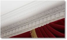 White decorative molding over a deep red curtain with gold fringe.