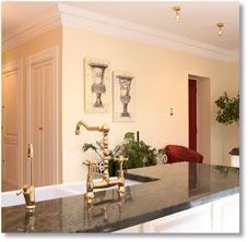 Kitchen with a black countertop, gold faucet, and cream-colored walls; includes decorative wall art and a view to another room.