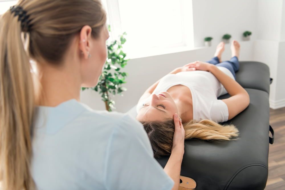 A Woman is Laying on a Table Getting a Head Massage From a Nurse — Sugarland Chiropractic Centre in Avoca, QLD