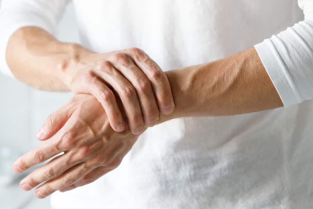 A Man is Holding His Wrist in Pain — Sugarland Chiropractic Centre in Avoca, QLD