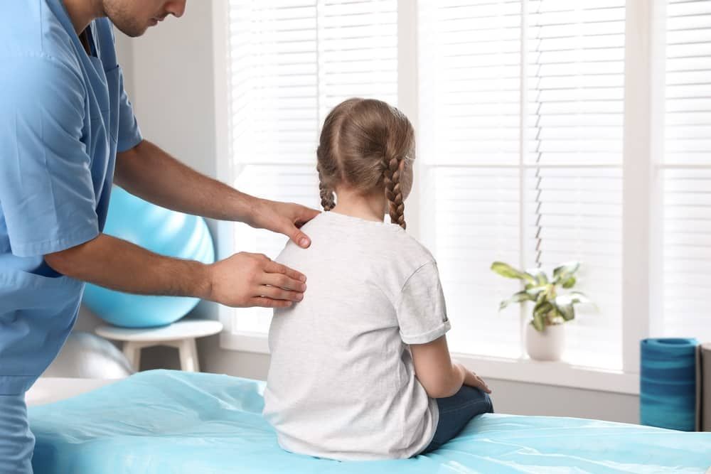 A Little Girl is Sitting on a Bed While a Doctor Examines Her Back — Sugarland Chiropractic Centre in Avoca, QLD