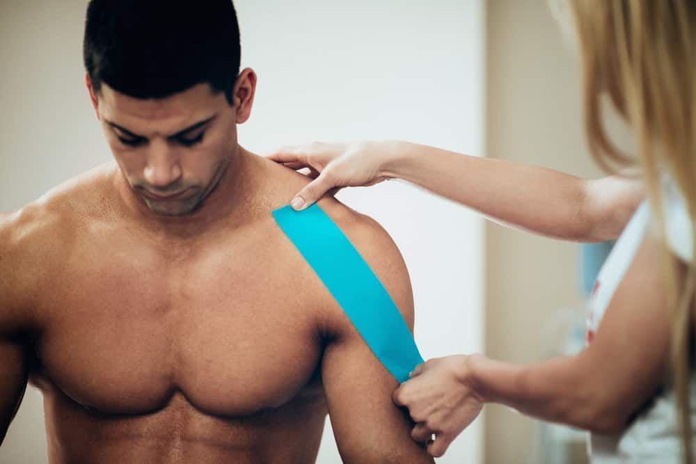 A Woman is Applying Kinesio Tape to a Man 's Shoulder — Sugarland Chiropractic Centre in Avoca, QLD