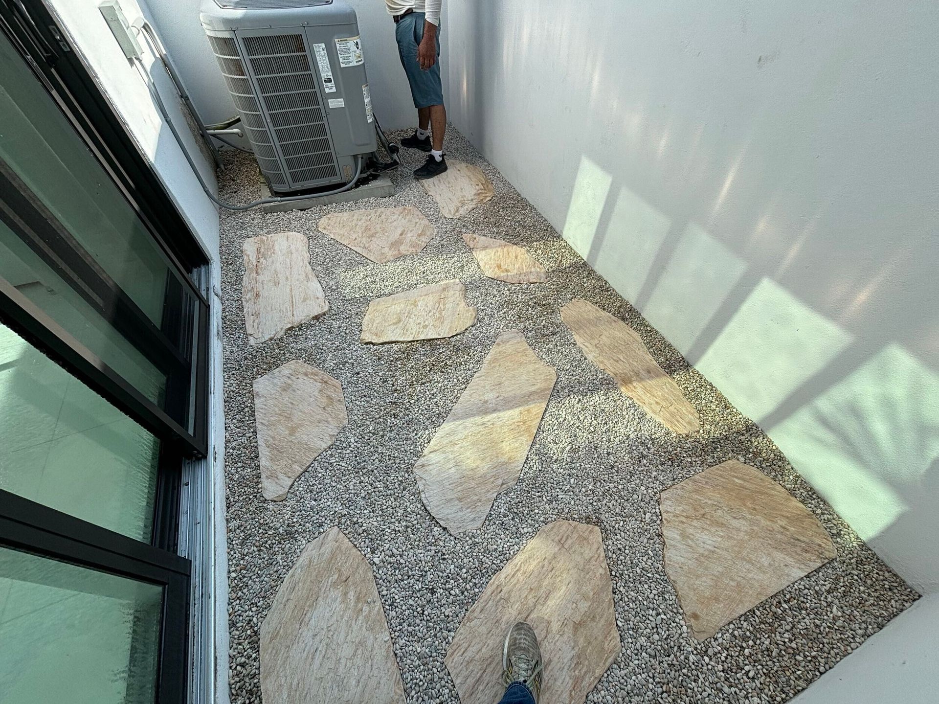 Narrow outdoor walkway with stepping stones and gravel; person standing near AC unit.