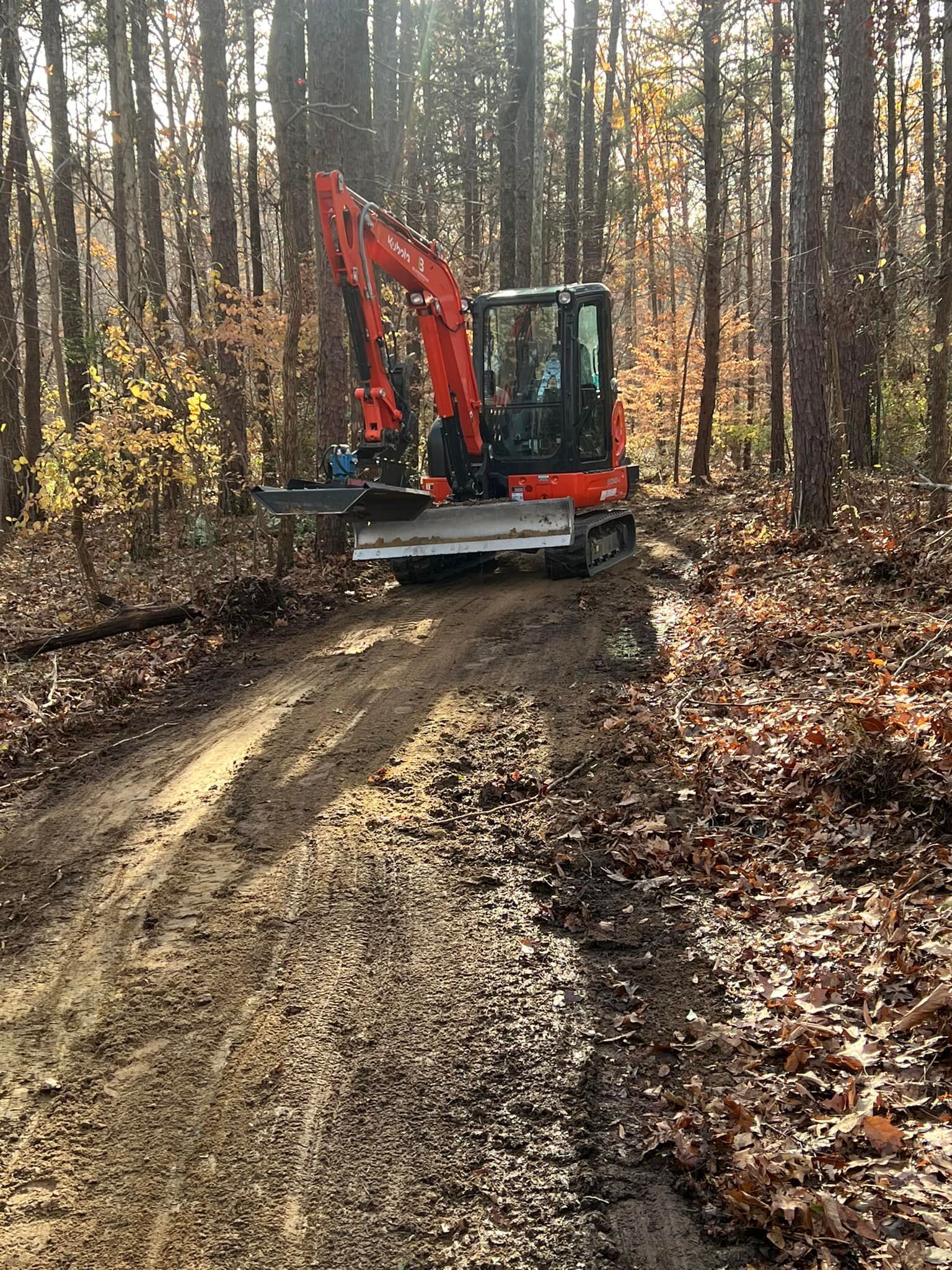 An excavator is driving down a dirt road in the woods.