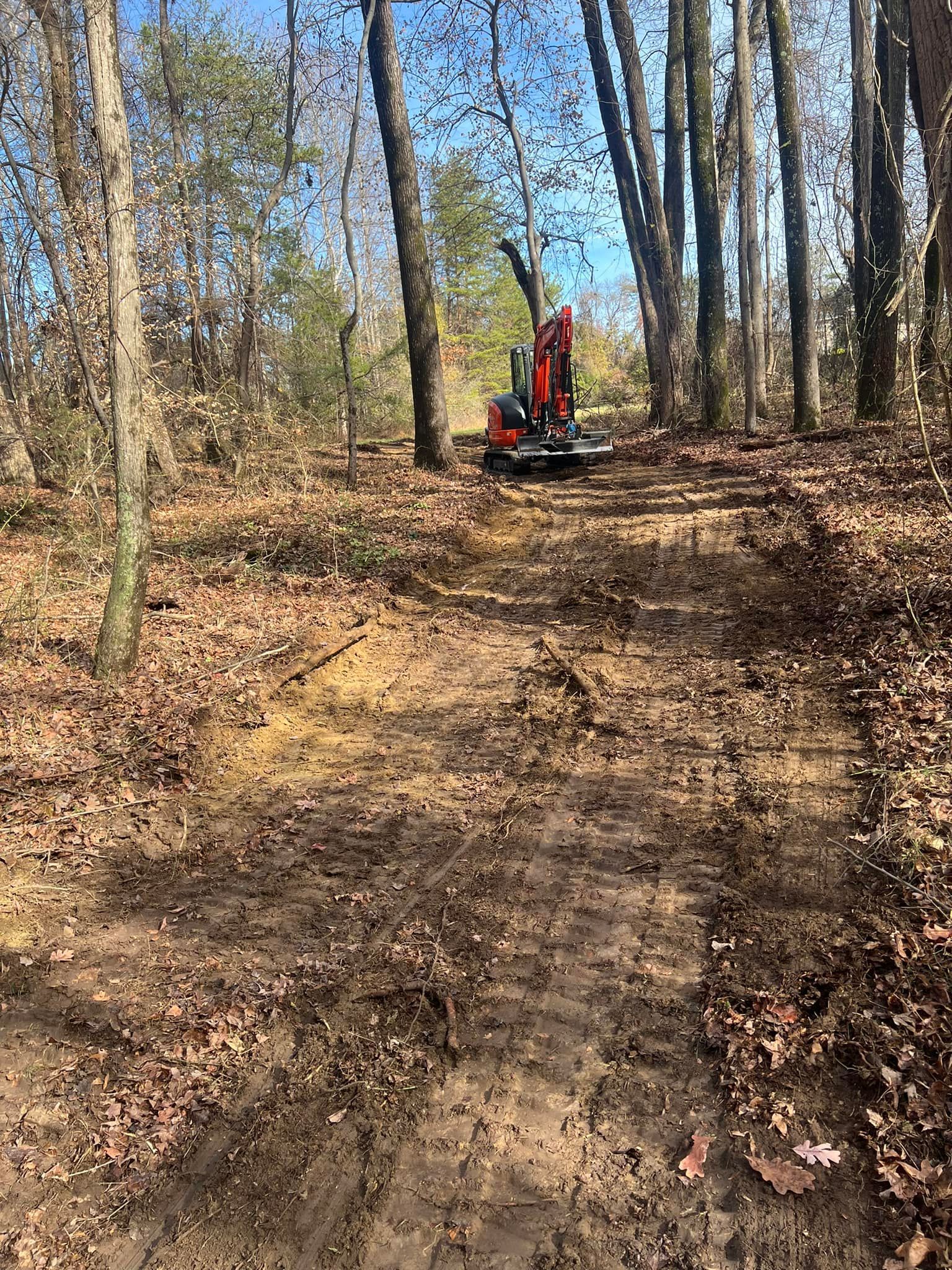 A tractor is driving down a dirt road in the woods.