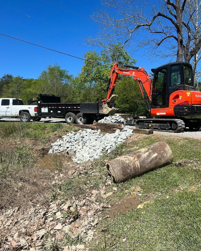 An excavator is digging a hole in the grass next to a truck.