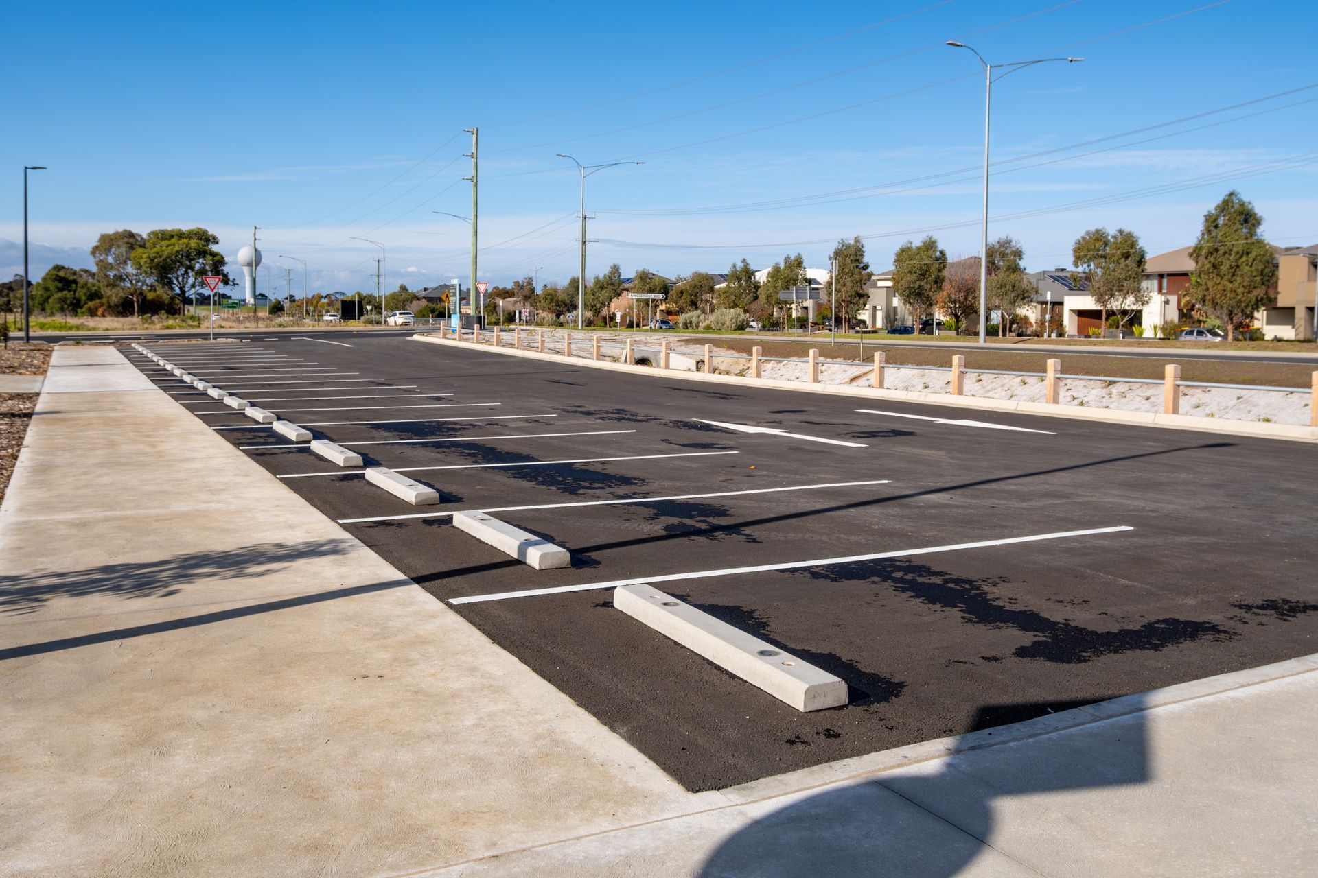 Empty parking lot with freshly painted white lines and concrete wheel stops under a clear sky