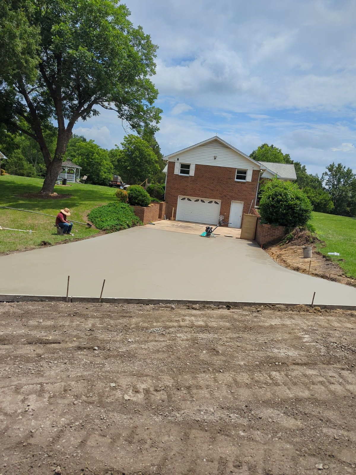 New concrete driveway leading to a brick garage, with a person sitting on the left lawn. New concrete driveway leading to a brick garage, with a person sitting on the left lawn.