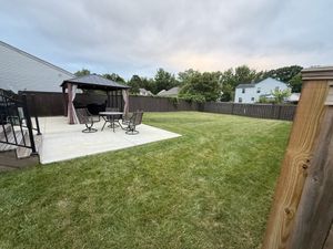 Backyard with patio, gazebo, table, chairs, and a wooden fence. Green grass and overcast sky.