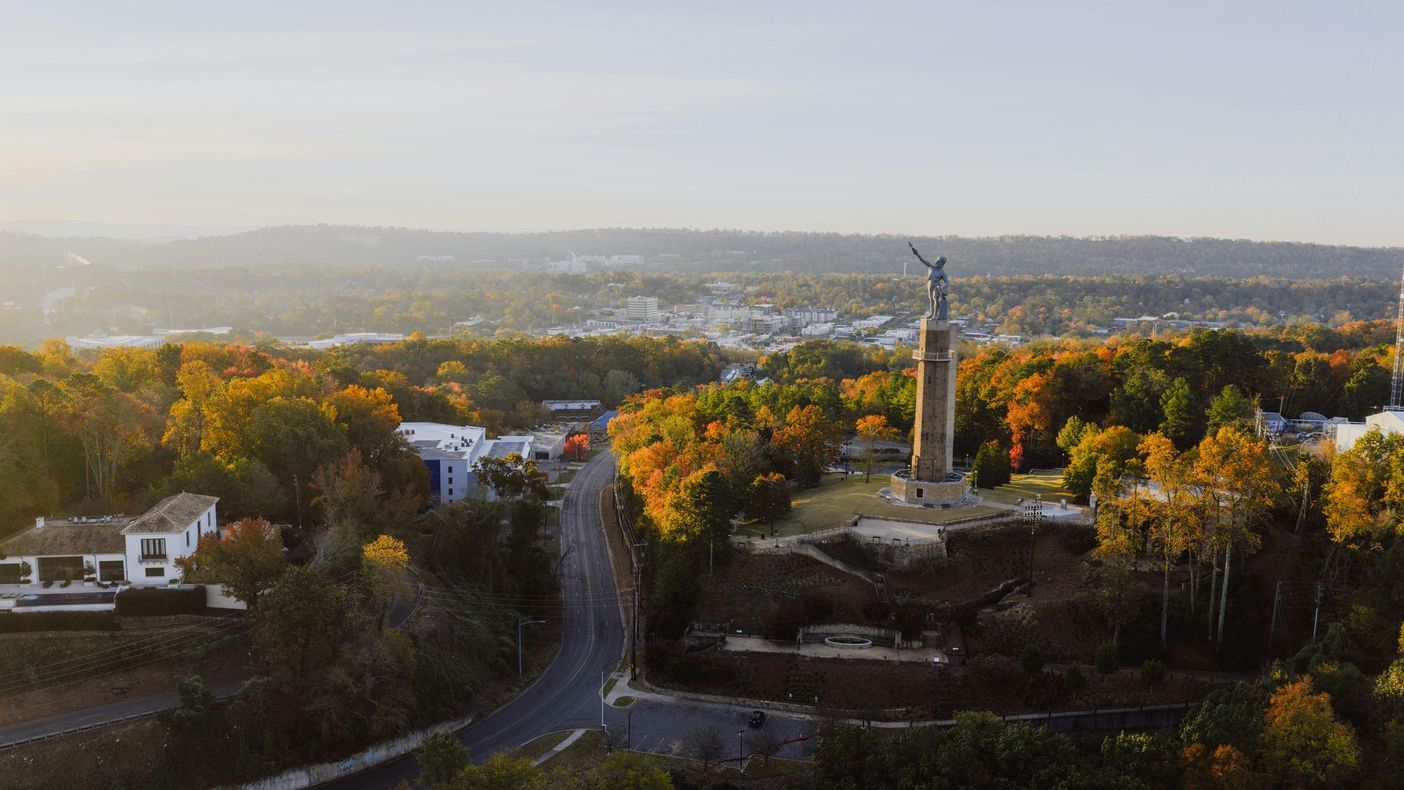 Aerial view of a tree-lined town road leading to a tall monument at sunset