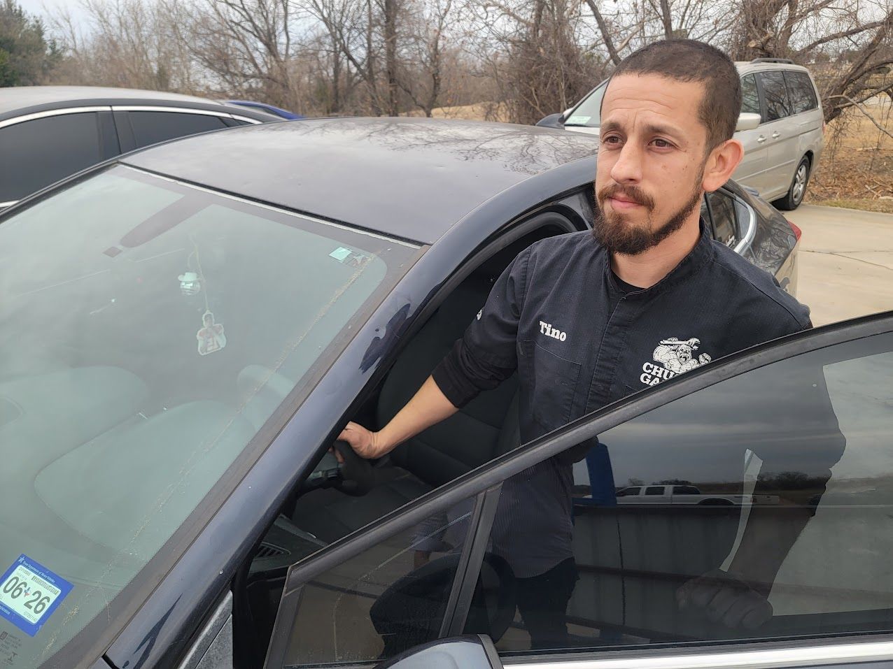 Man exiting a black car, holding the door open. He has a beard and is outside.
