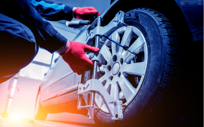Mechanic in red gloves adjusting car wheel alignment with white equipment.