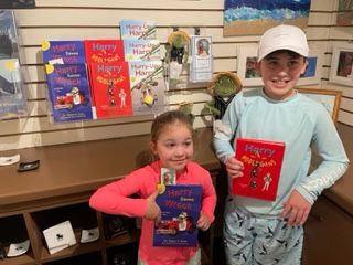Two children holding copies of a book, "Harry the Sea Turtle". Books and display in a shop.