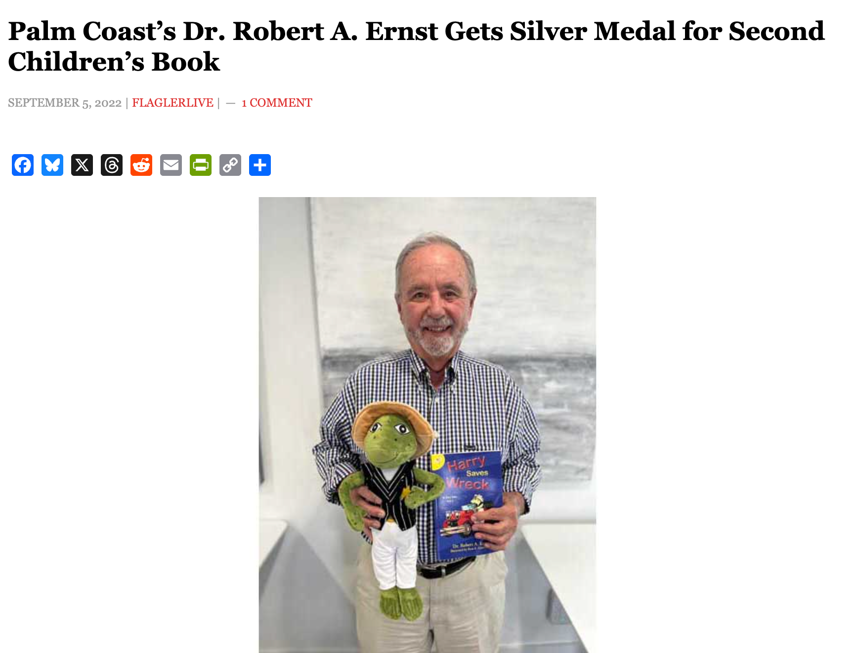 Dr. Robert A. Ernst holds a book and a frog stuffed toy, smiling.