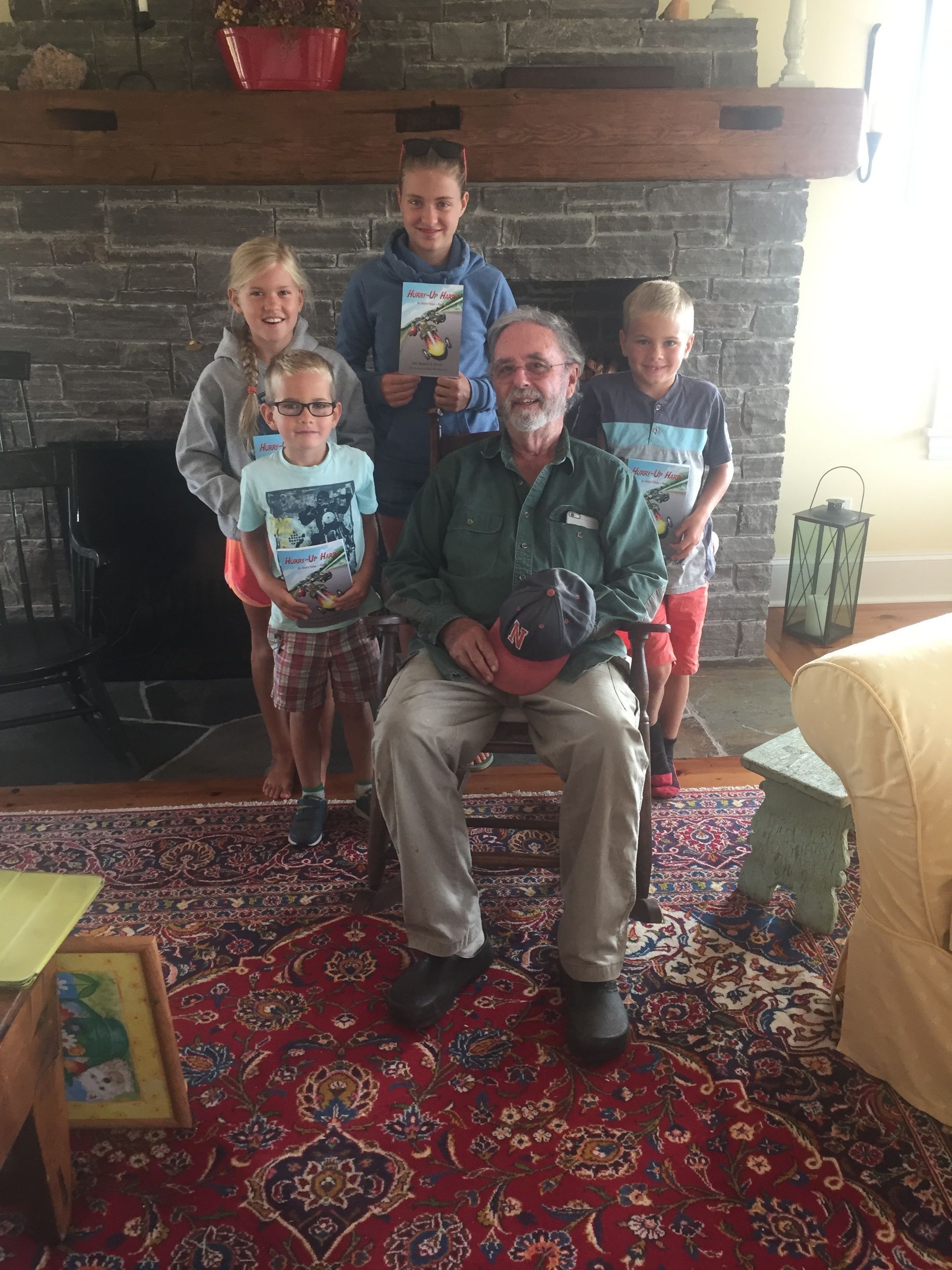 Man seated with four children in front of a stone fireplace. All are smiling, posing.