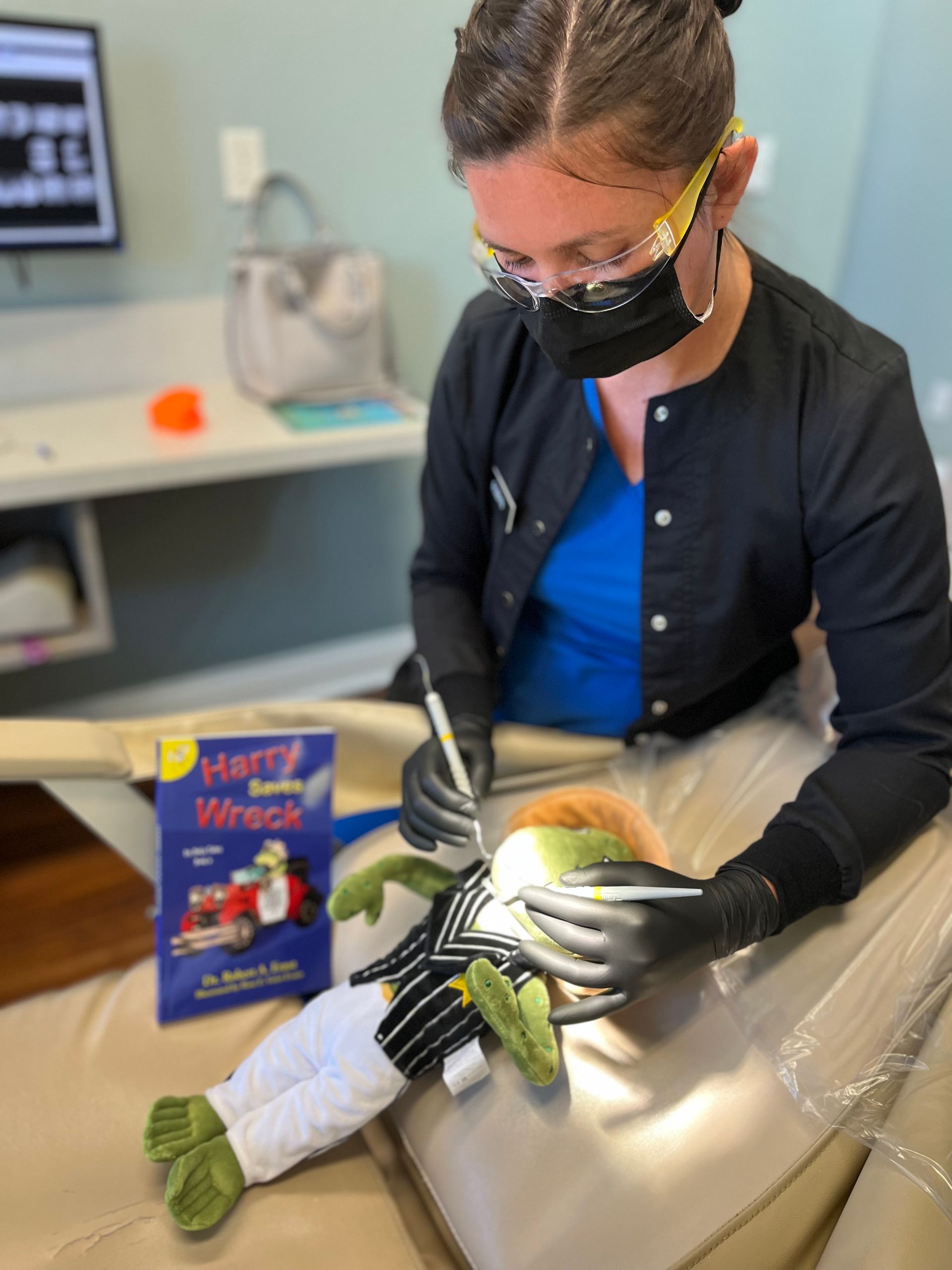 Dentist examining a plush toy in a dental chair. A book titled