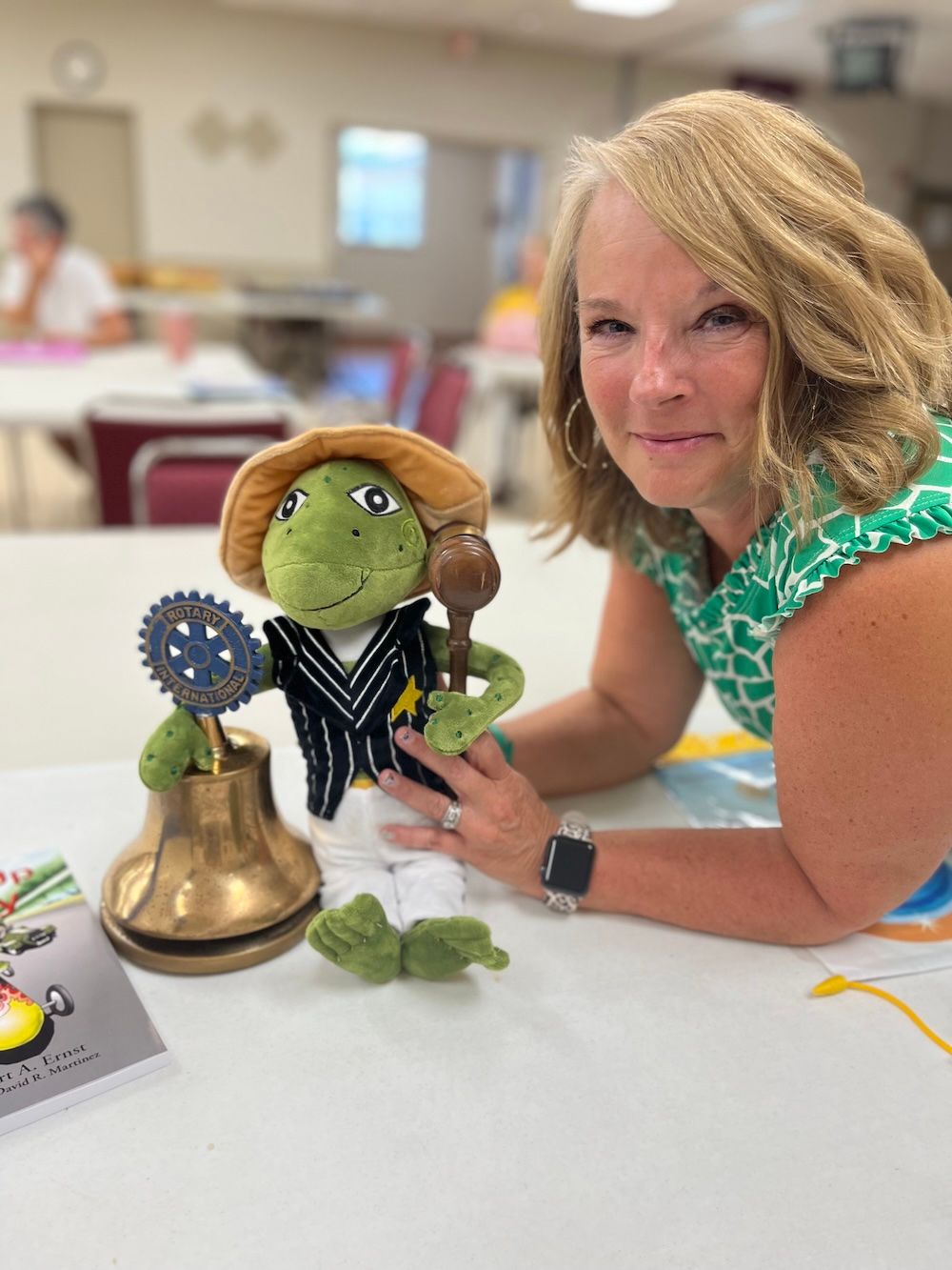 Stuffed green frog in a straw hat and striped vest, posing in white pants.