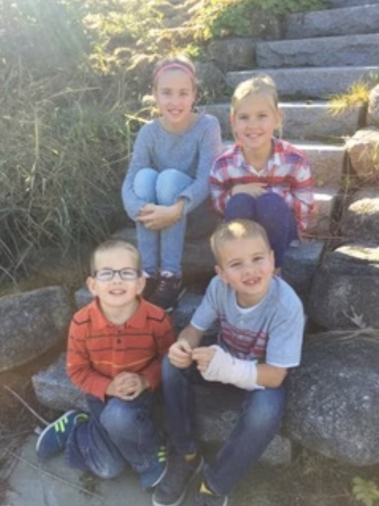 Four children sitting on stone steps outside.