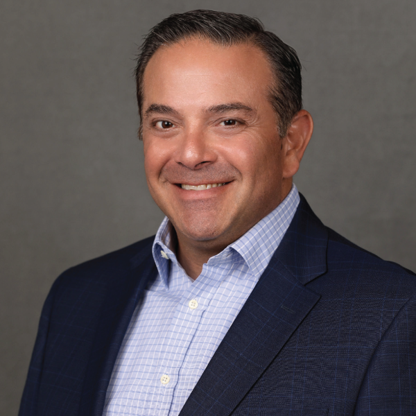 Smiling professional in a navy blazer and light blue shirt against a gray studio background