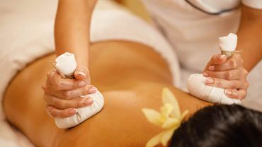 Las manos masajean la espalda de la persona con piedras calientes y toallas blancas.