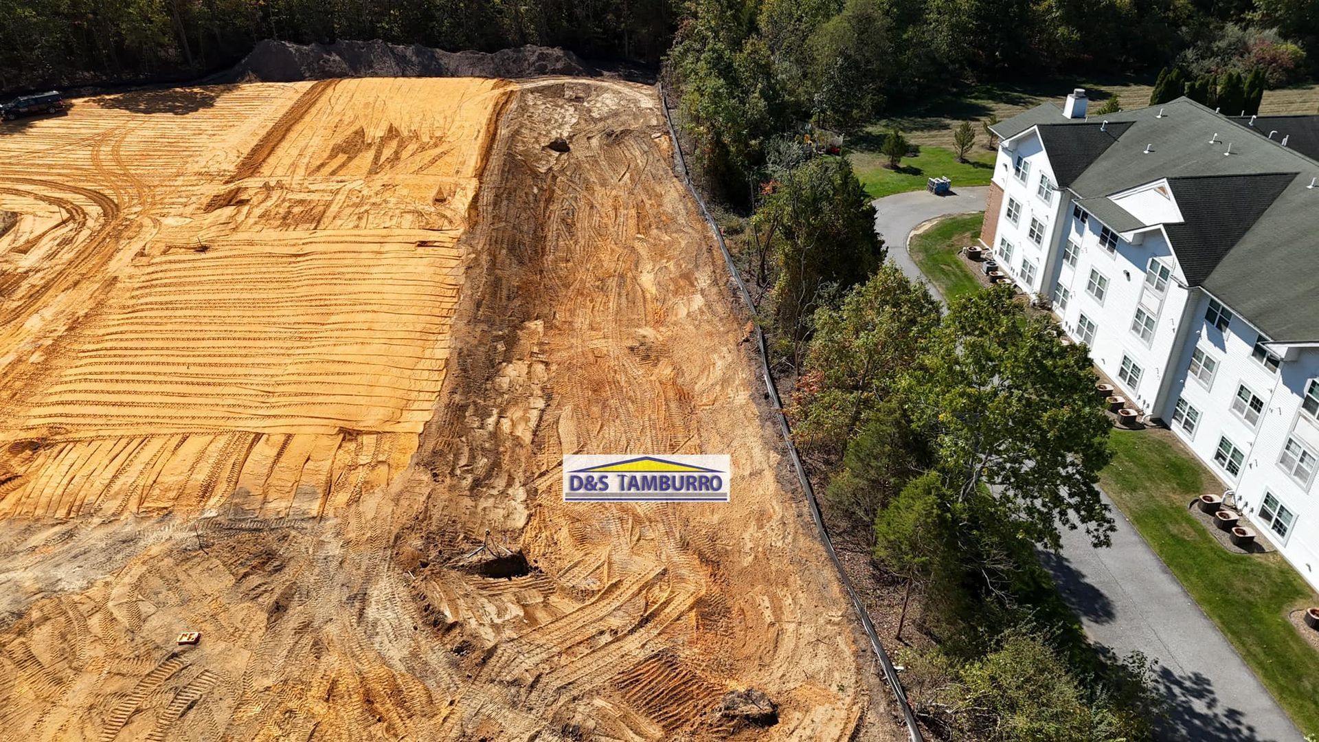 Aerial view of a construction site next to a building and trees; earth is exposed in various stages of clearing.