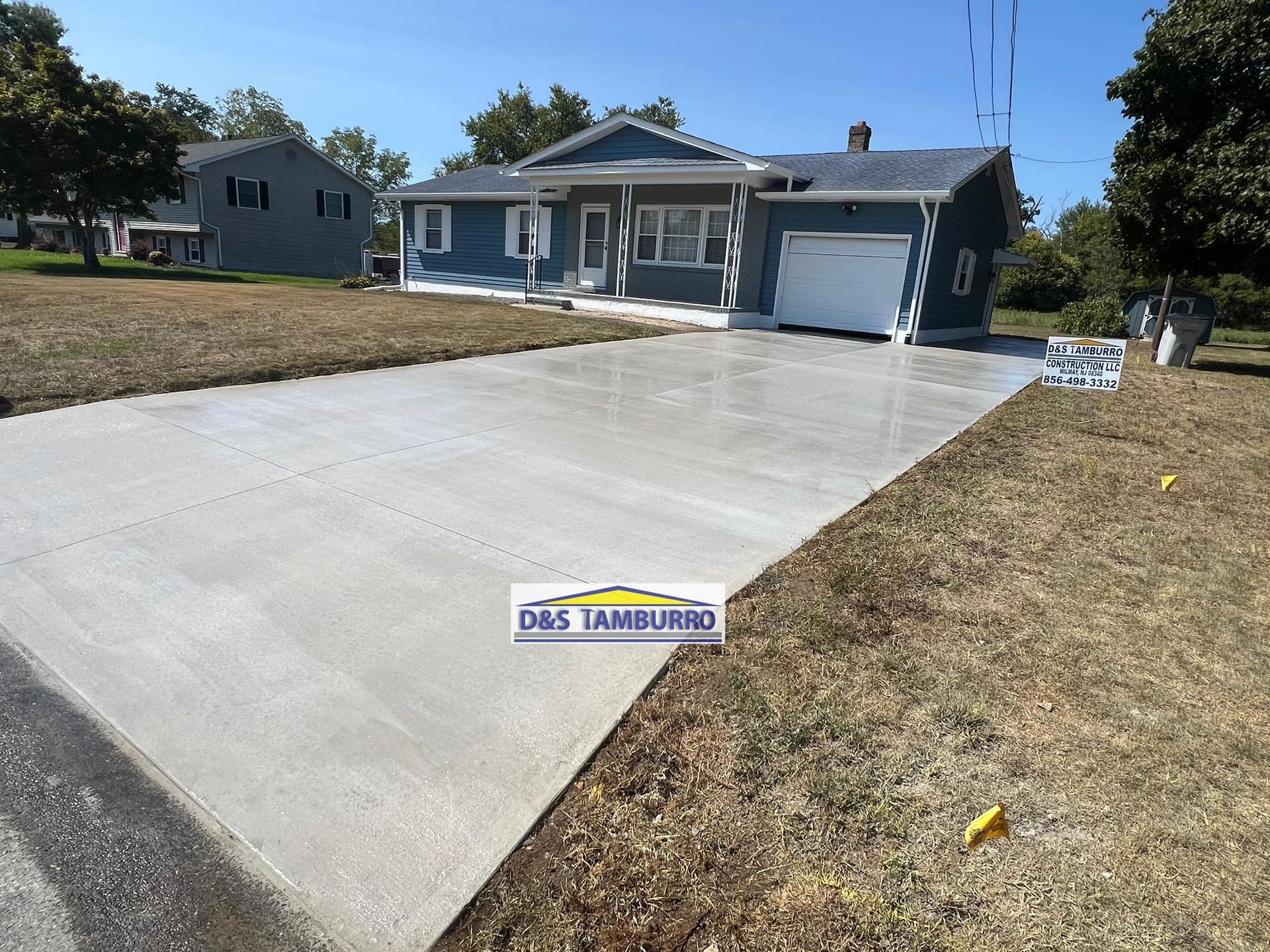 Freshly poured concrete driveway leading to a blue house with a white garage door.