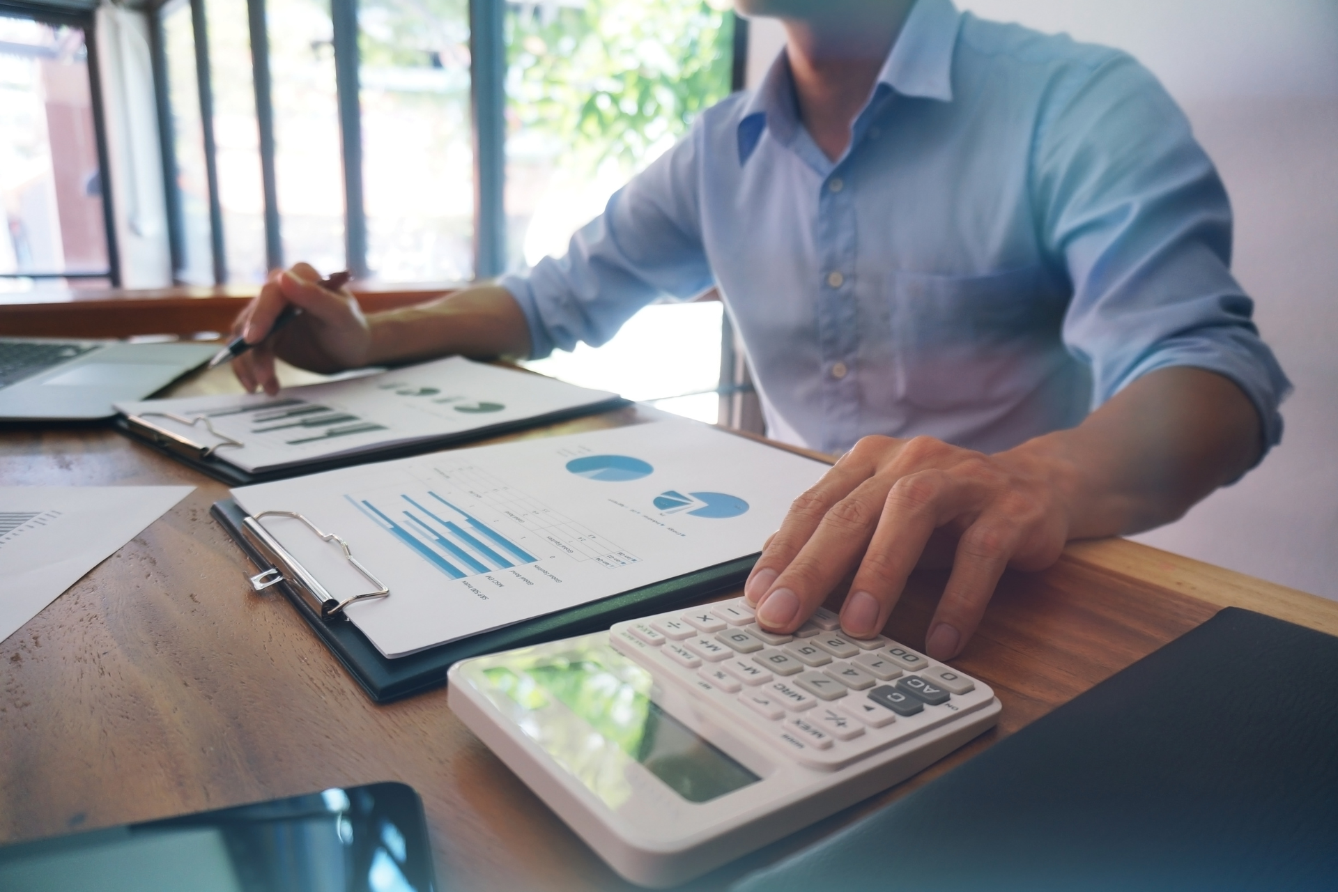 Person reviewing charts with calculator and clipboard at a desk in a bright office