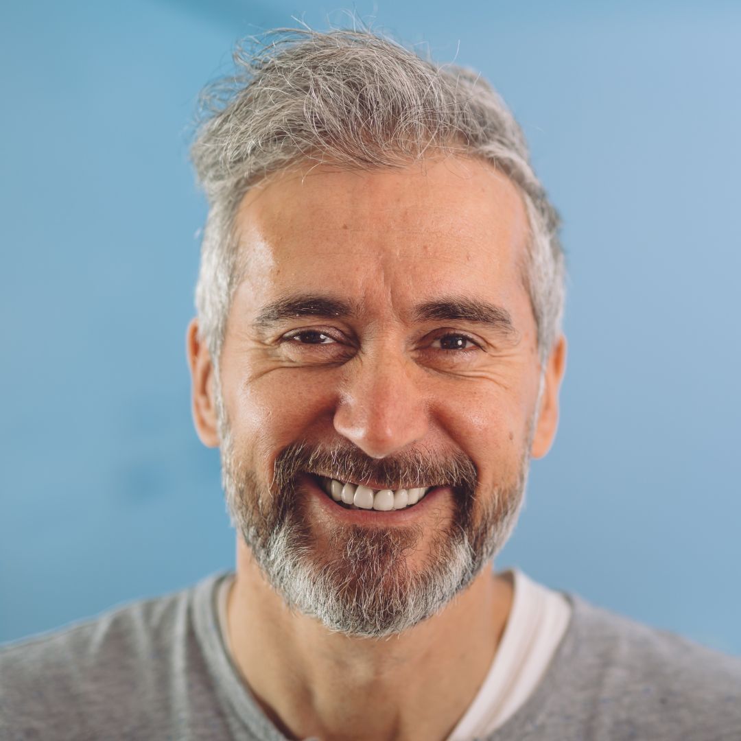 Smiling gray-bearded man in a gray shirt against a blue background