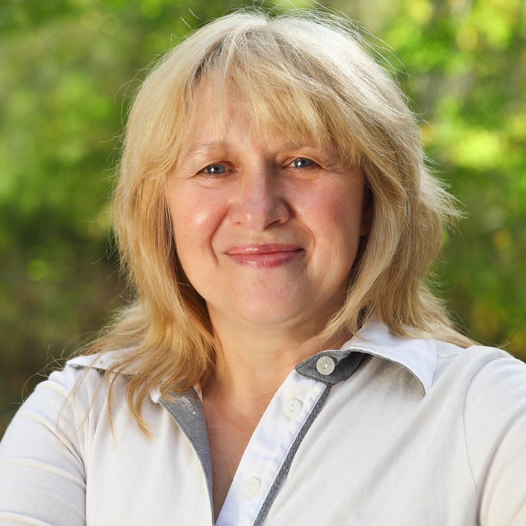 Smiling blonde woman in a white shirt outdoors with a blurred green background
