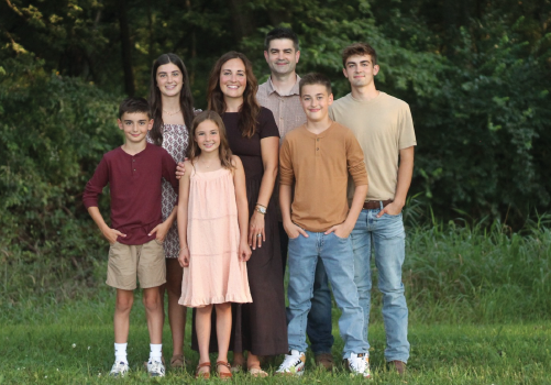Five people standing outdoors in a grassy area, smiling at the camera.
