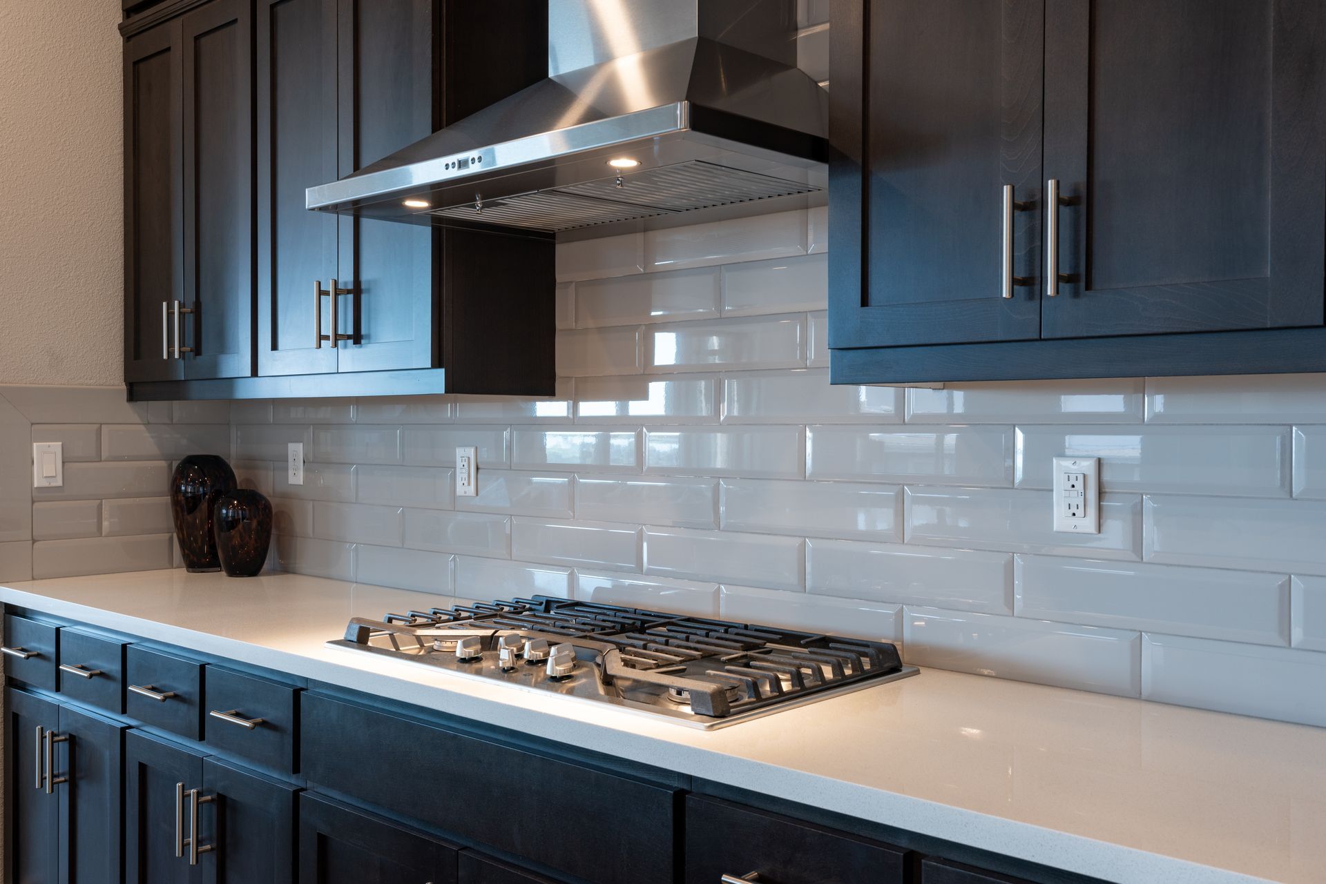 A modern kitchen with dark wood cabinets, a white quartz countertop, a gas cooktop, and a glossy gray subway tile backsplash.