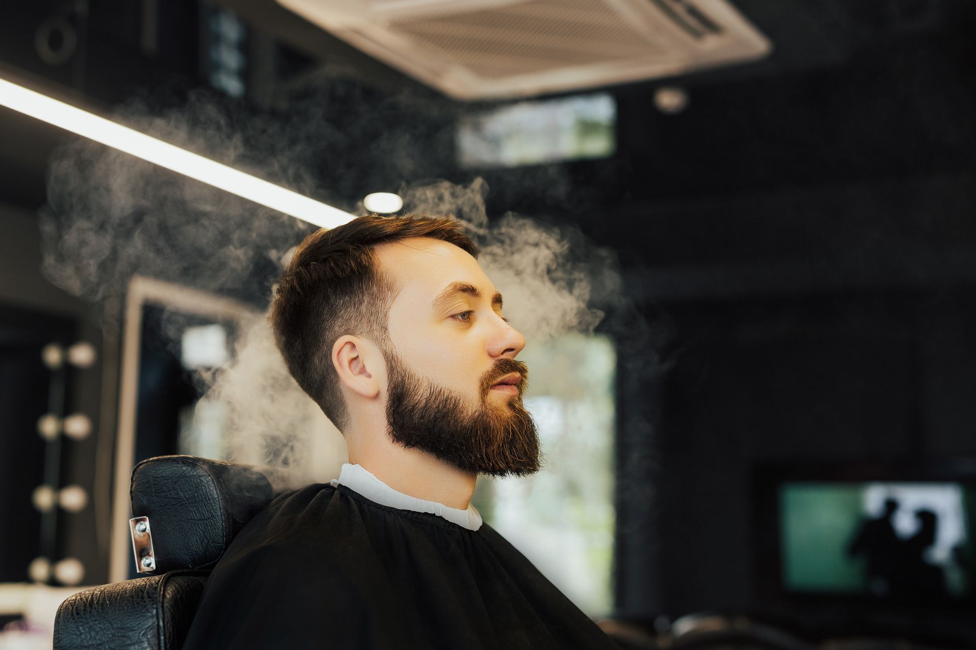 A man with a beard is sitting in a barber chair with his eyes closed.
