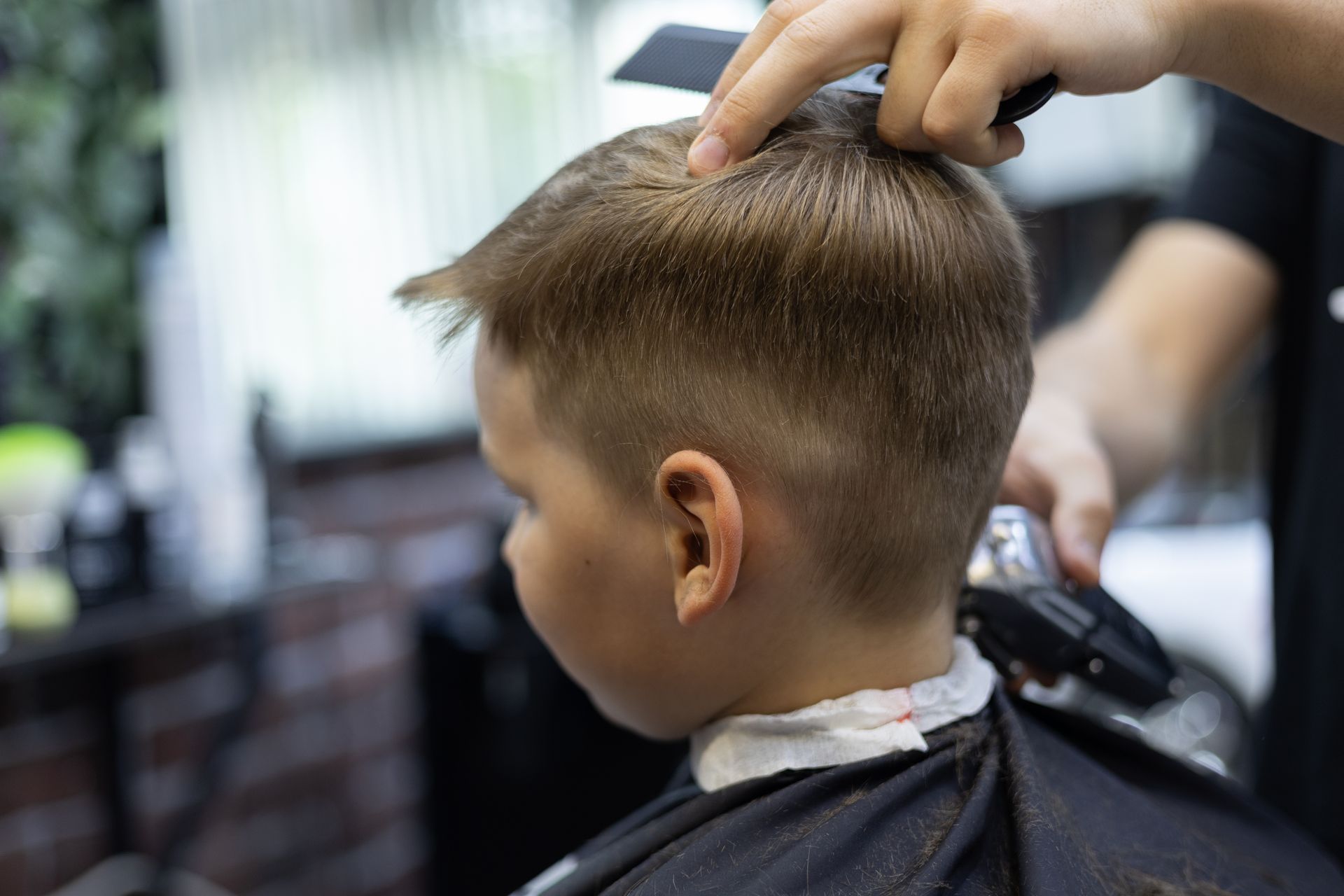 A young boy is getting his hair cut by a barber in a barber shop.