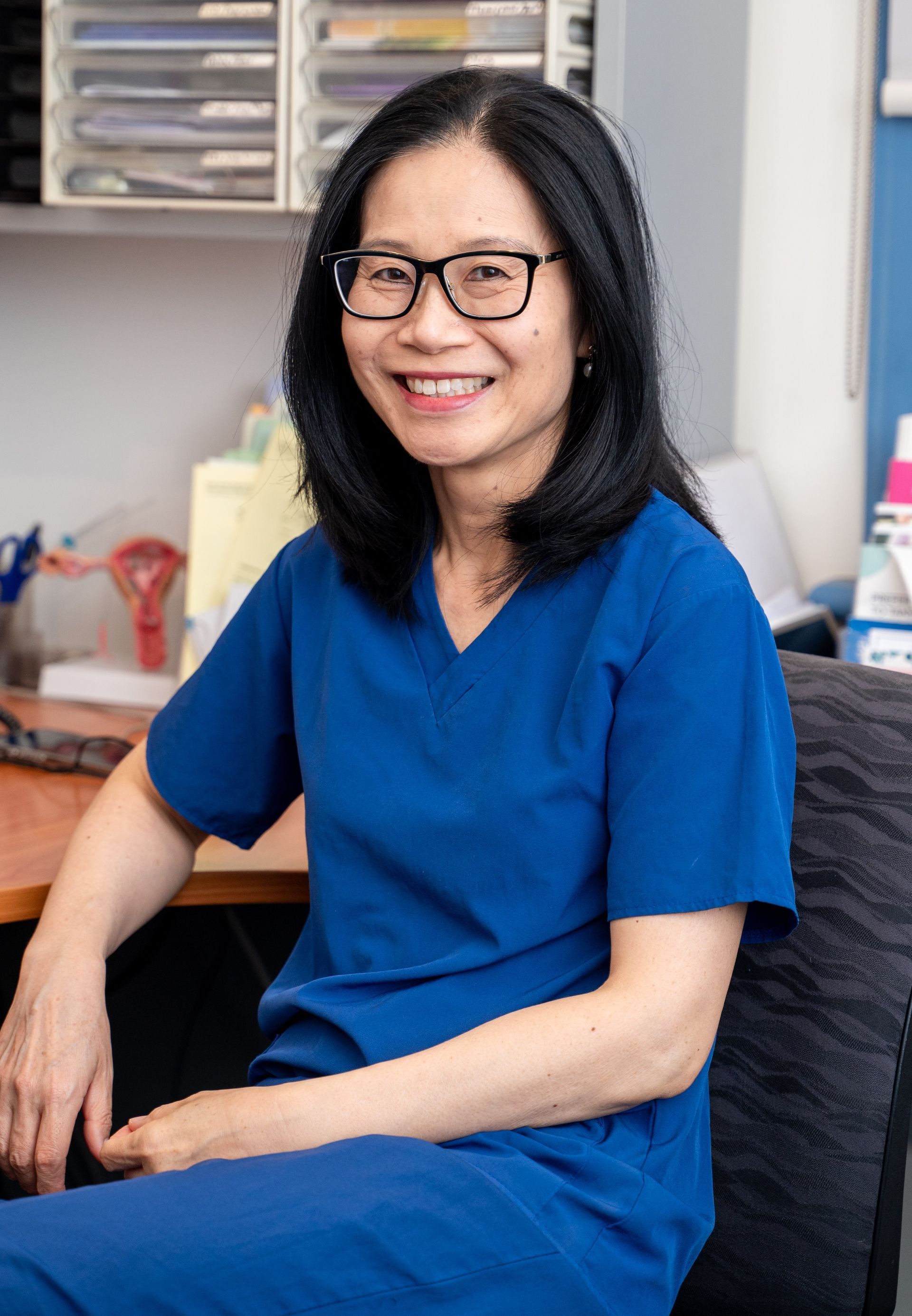 Smiling woman in blue scrubs seated in a clinical office setting