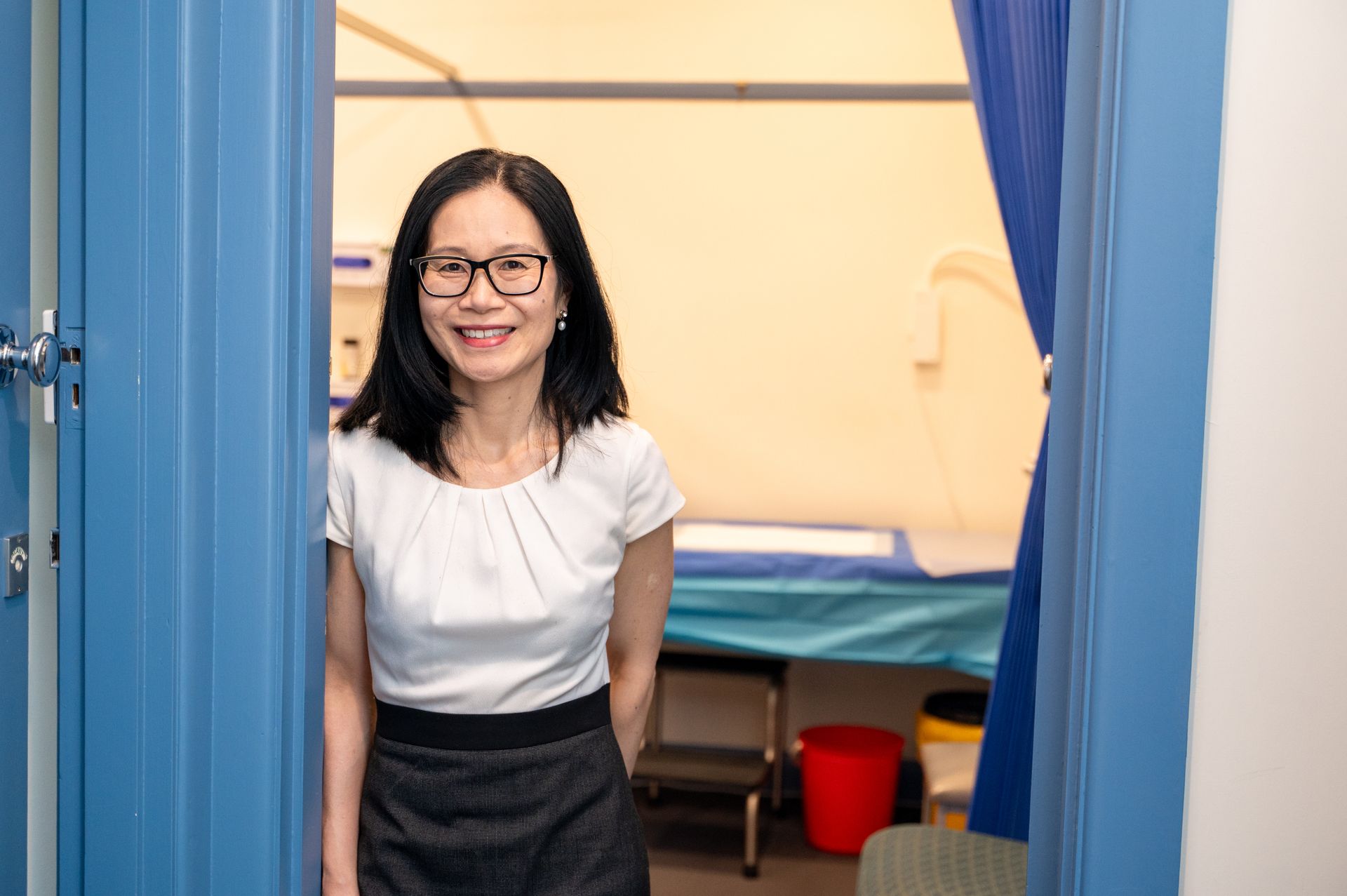 Woman smiling in a blue doorway, with a bed and lamp visible in the room behind her