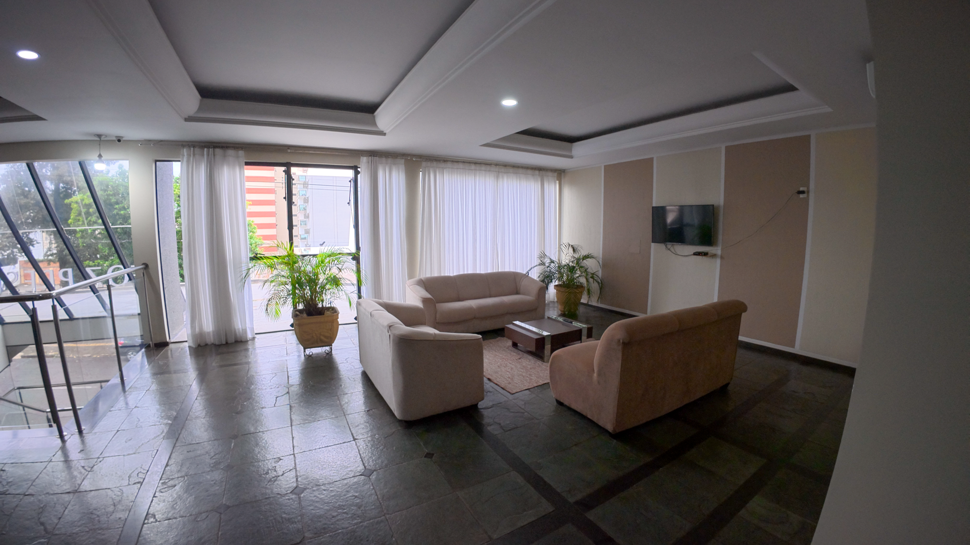 Sala de estar moderna com sofás bege, plantas em vasos e grandes janelas com vista para a vegetação.