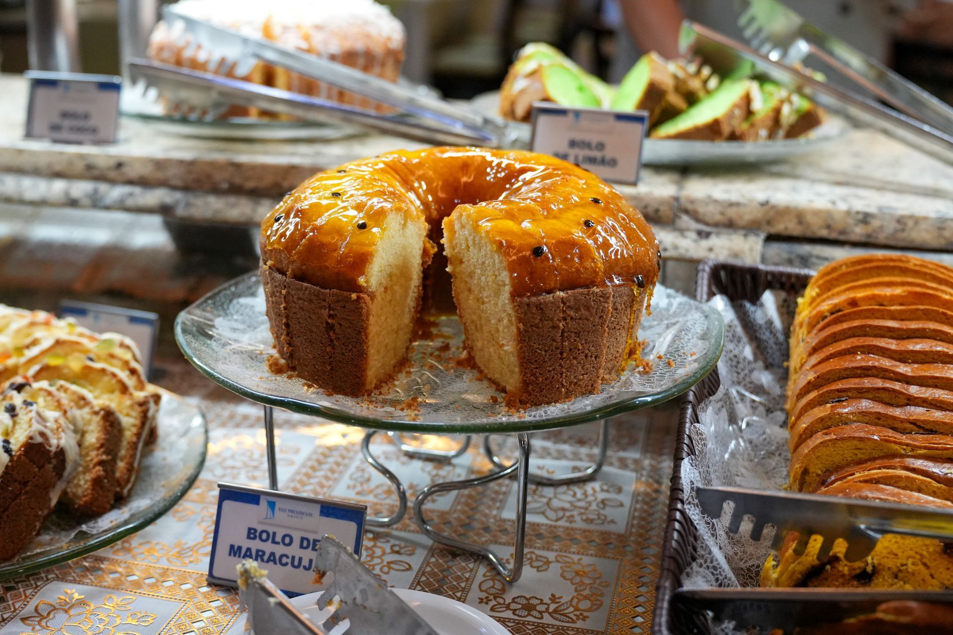 Variedade de doces expostos em uma padaria, incluindo um bolo Bundt com cobertura e fatias de pão.