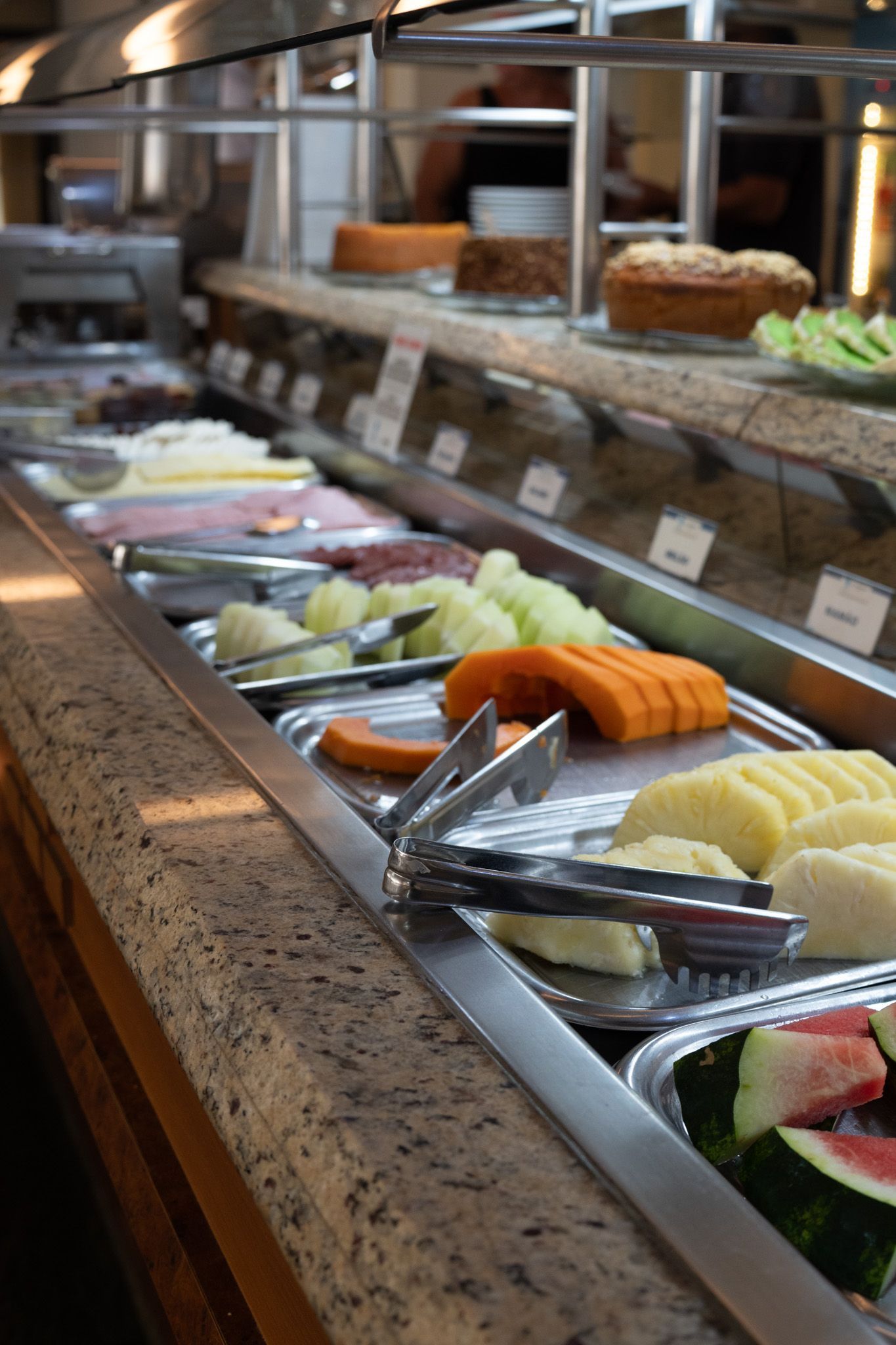 Buffet de sushi e sashimi com pinças e bandejas sob cobertura de vidro