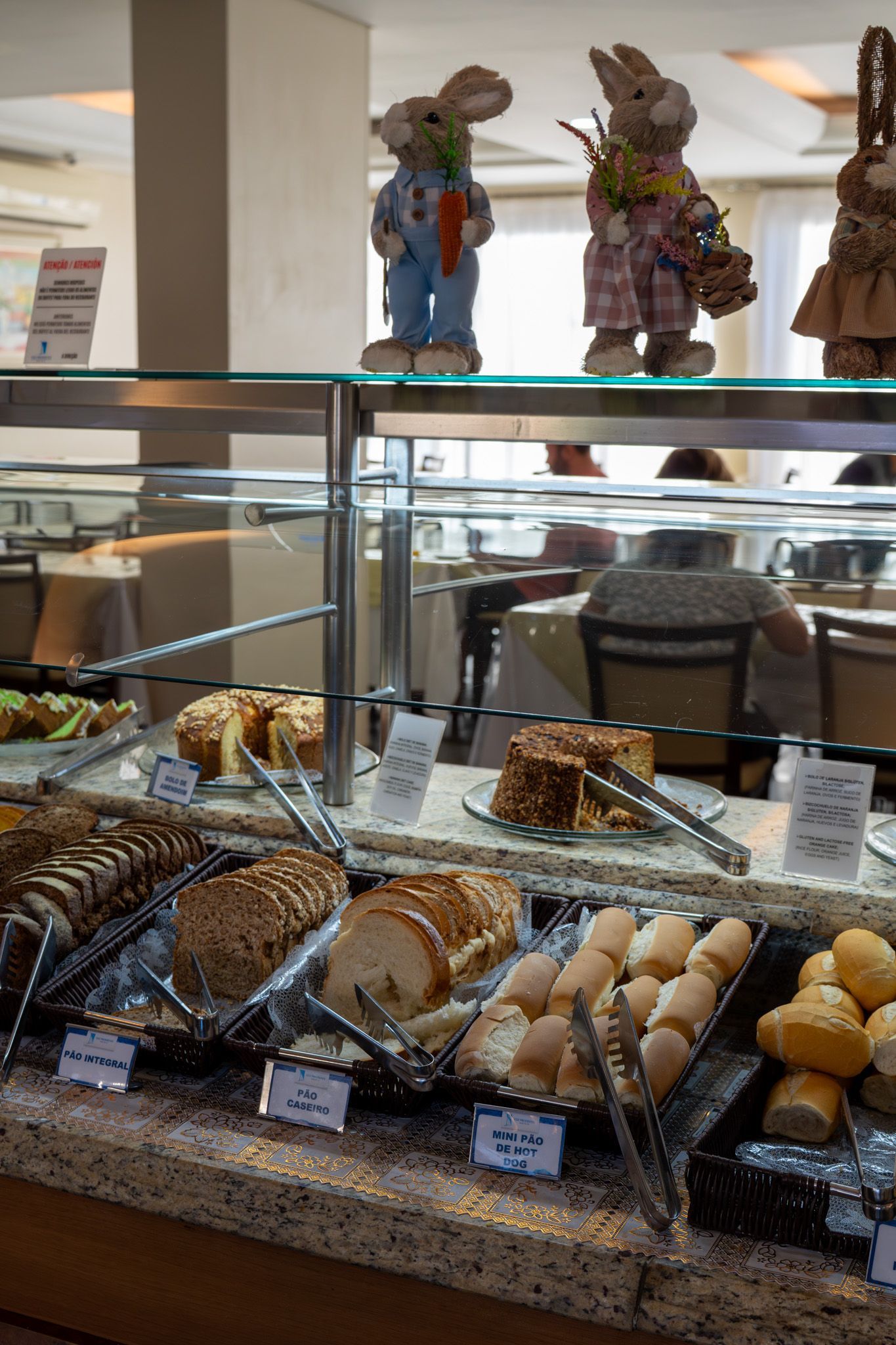 Vitrine de padaria com uma variedade de doces e três figuras decorativas no topo.