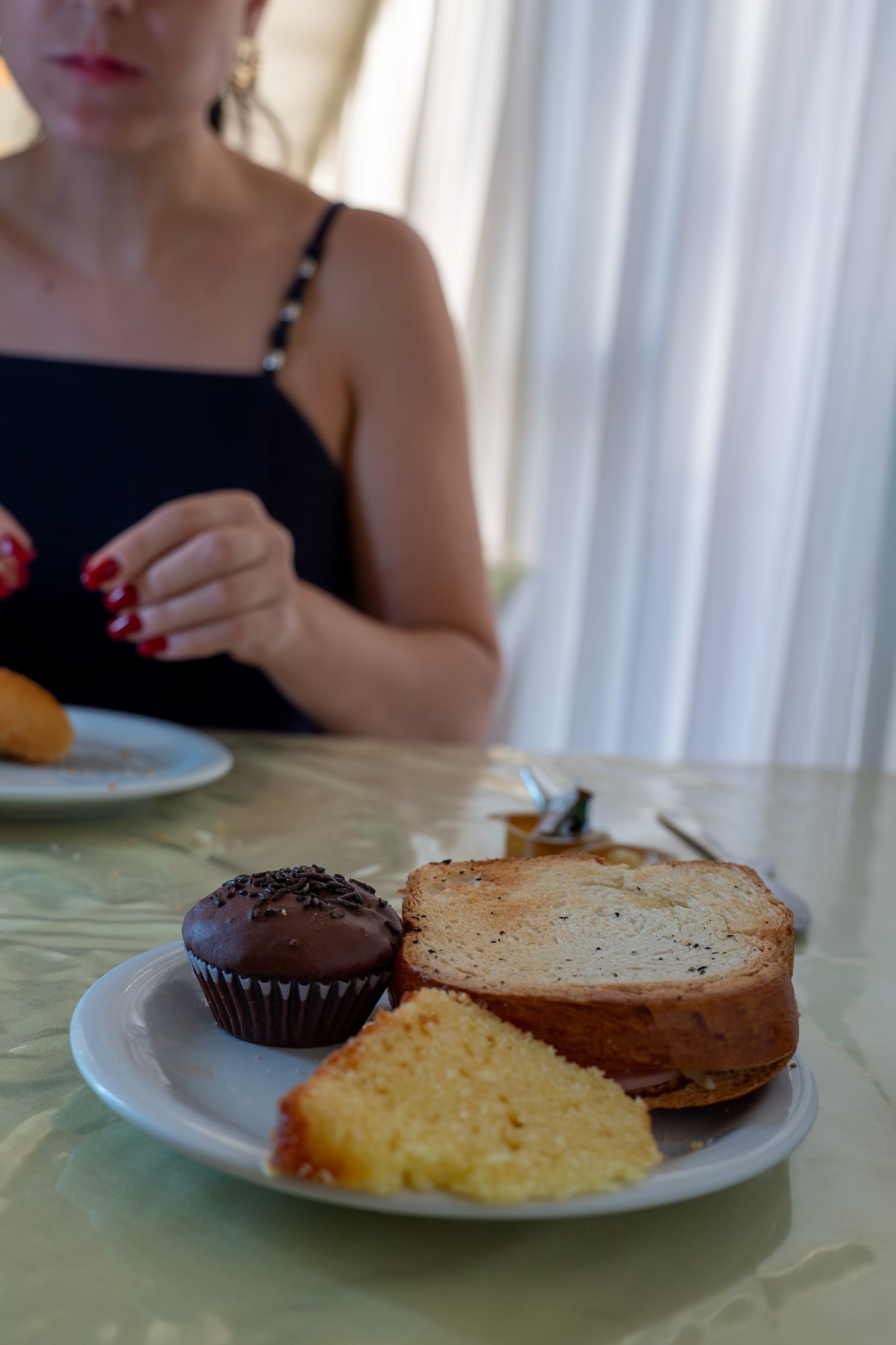Prato com fatias de bolo e cupcake de chocolate sobre uma mesa ao lado de uma pessoa sentada à mesa de jantar.