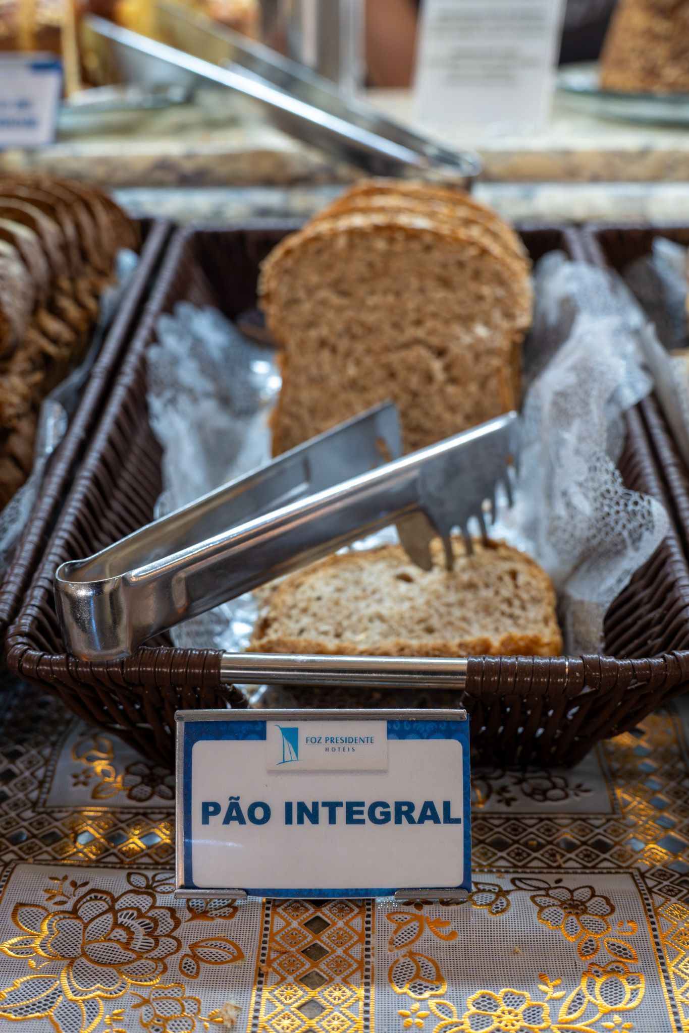 Cesta de pão integral fatiado com a etiqueta “Pão Integral” em uma mesa de buffet.