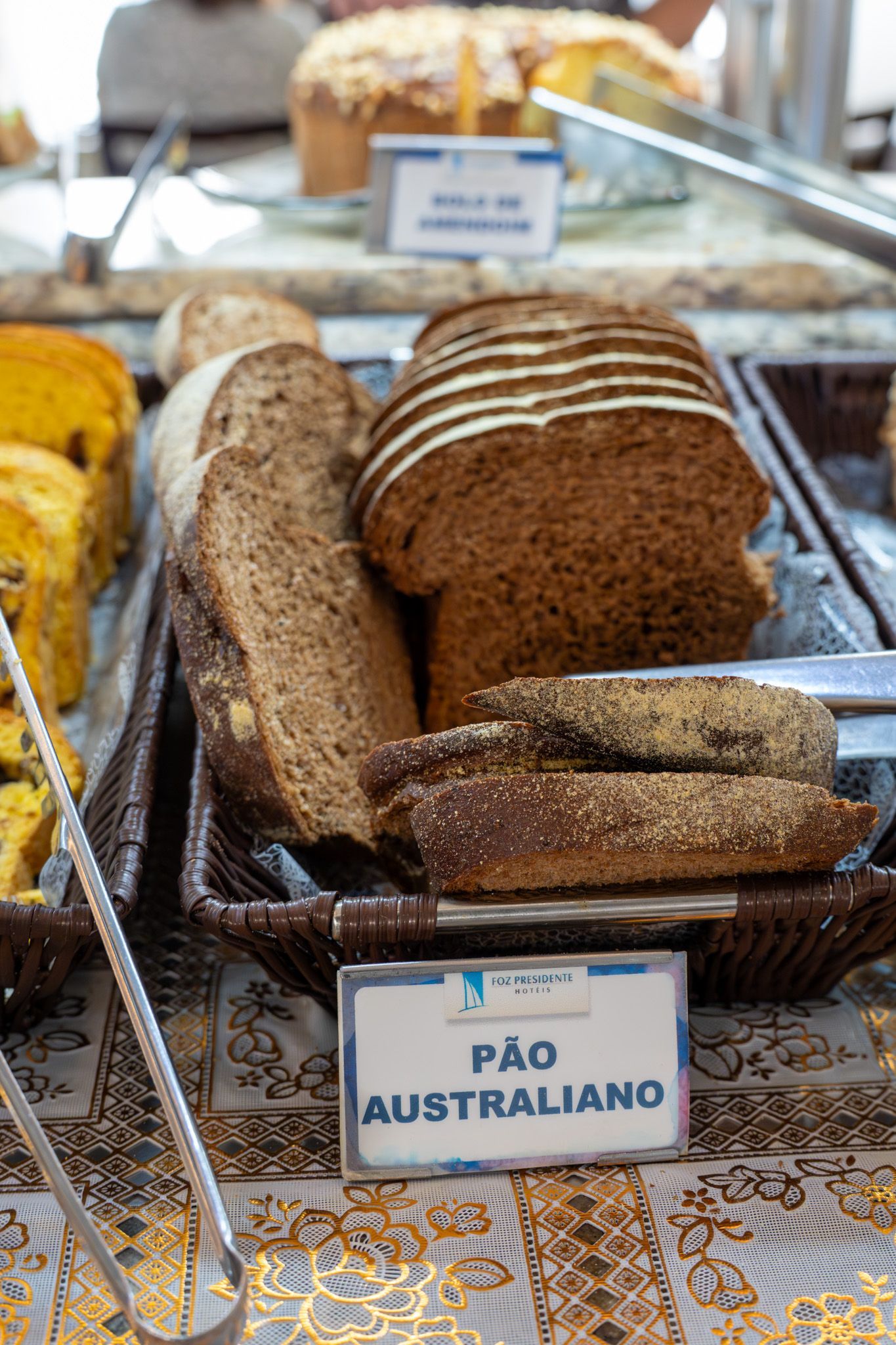 Bandeja com fatias de pão e pães inteiros em exposição numa padaria, com a etiqueta “Pão Australiano”.