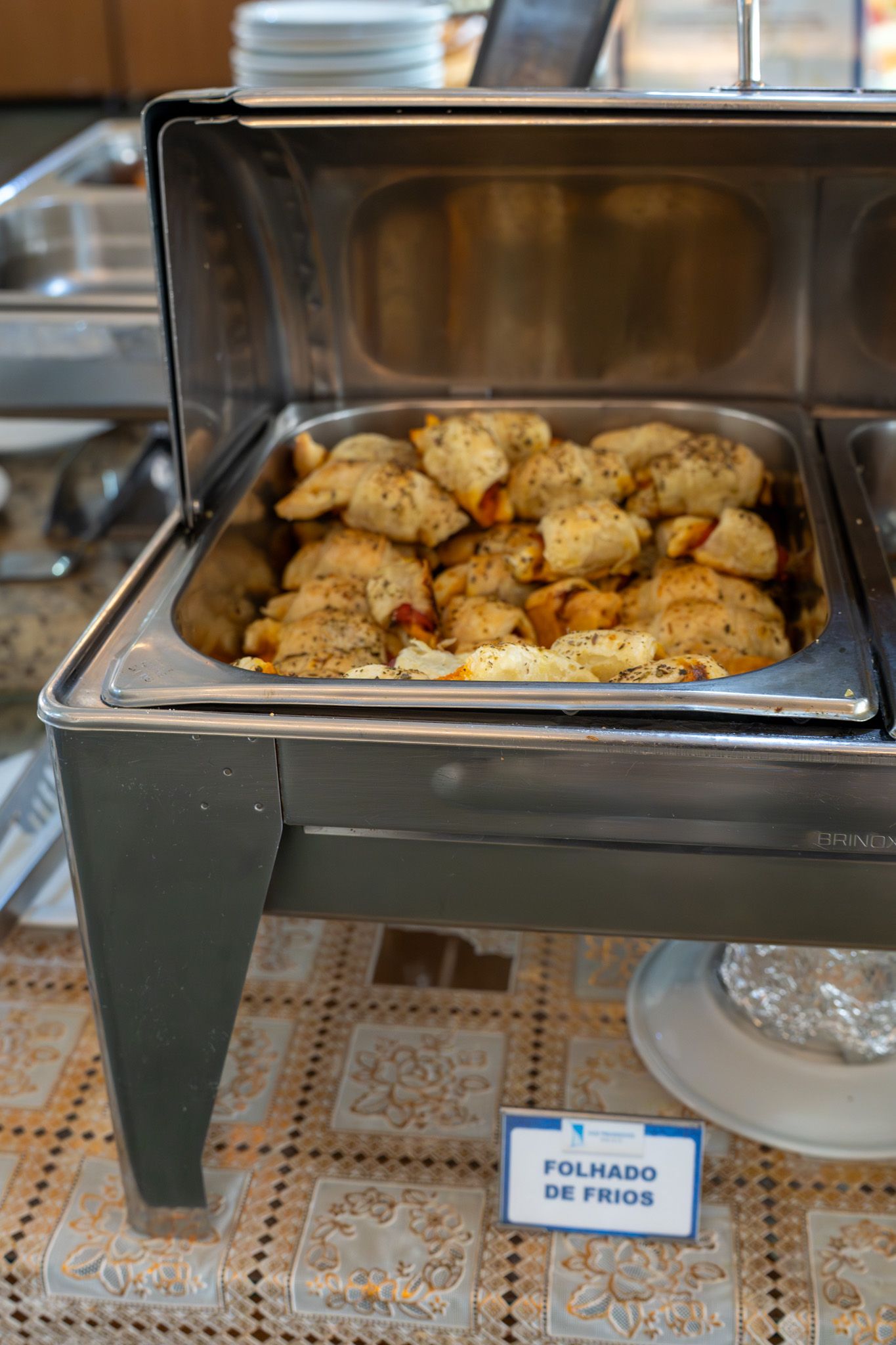 Mesa de vapor com pãezinhos assados em uma bandeja de bufê sobre uma toalha de mesa estampada.