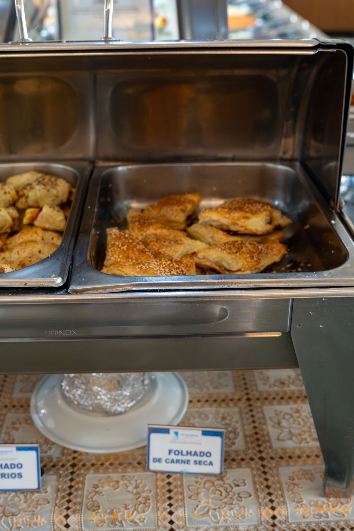 Bandeja de alimentos fritos em um expositor de bufê de aço inoxidável, com etiquetas abaixo.