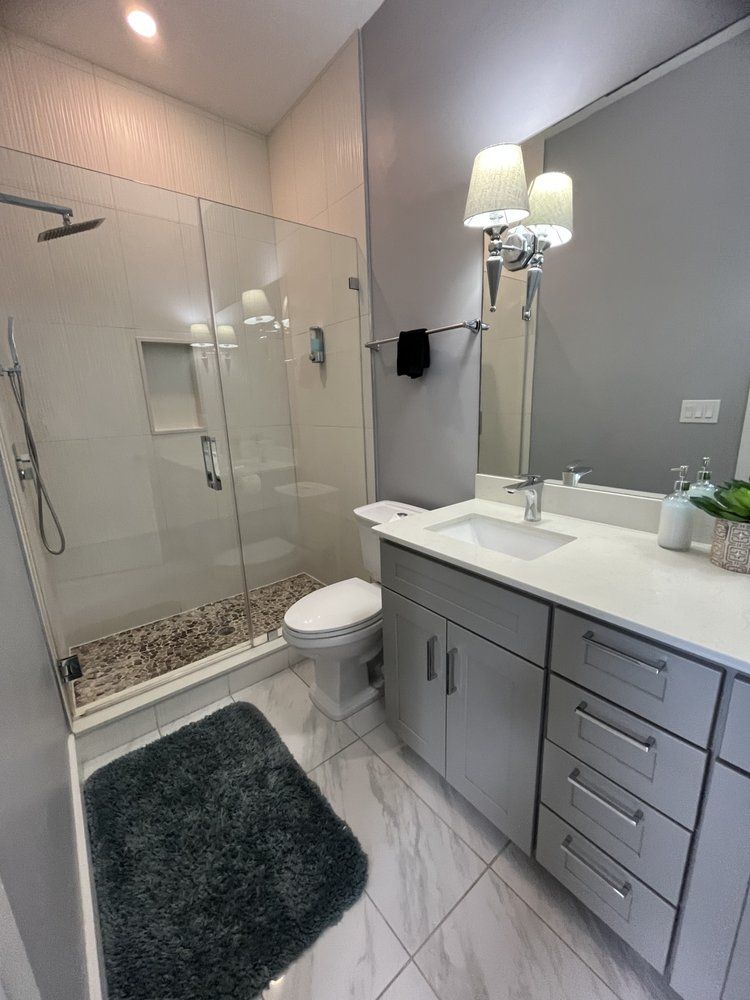A bathroom with a toilet , sink , shower and mirror.