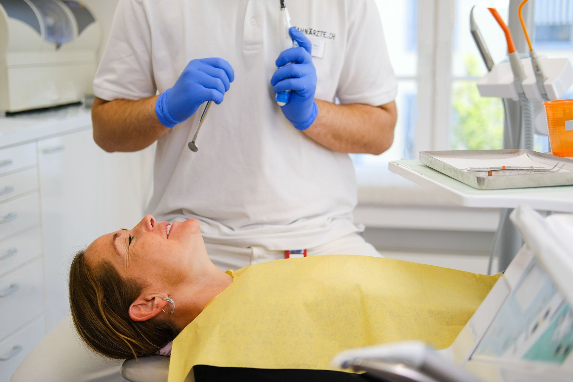A woman is laying in a dental chair while a dentist holds a syringe.